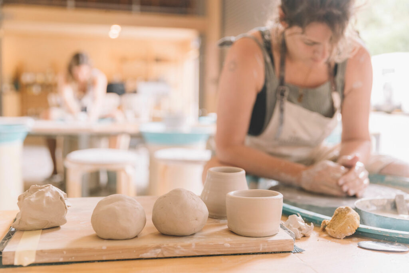 Student throwing pottery on the wheel with finished pieces nearby, Nambour