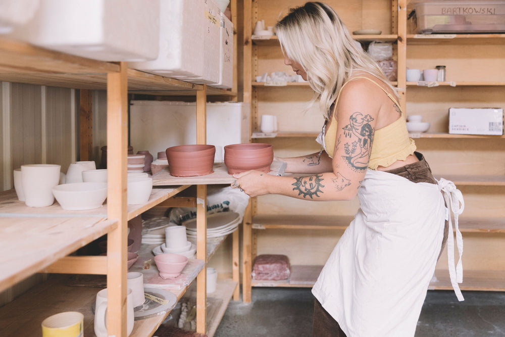 Student placing finished pottery pieces on shelves after wheel throwing class, Nambour Sunshine Coast