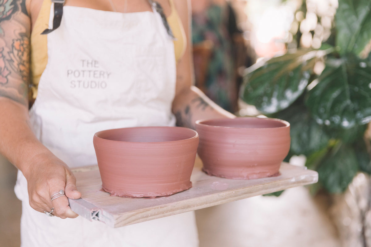 Student in The Pottery Studio apron holding two large clay bowls thrown on the pottery wheel, Nambour Sunshine Coast